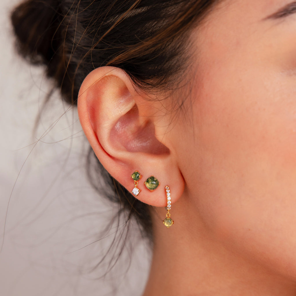 Close-up of an ear wearing the Agate Earrings Set—three green gemstone studs and a dangling earring with a green stone accented by small diamonds.