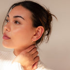 Woman with pierced ears wearing a white top looks to the side, hand touching her neck, highlighting the Diamond Earrings Set in soft natural light.