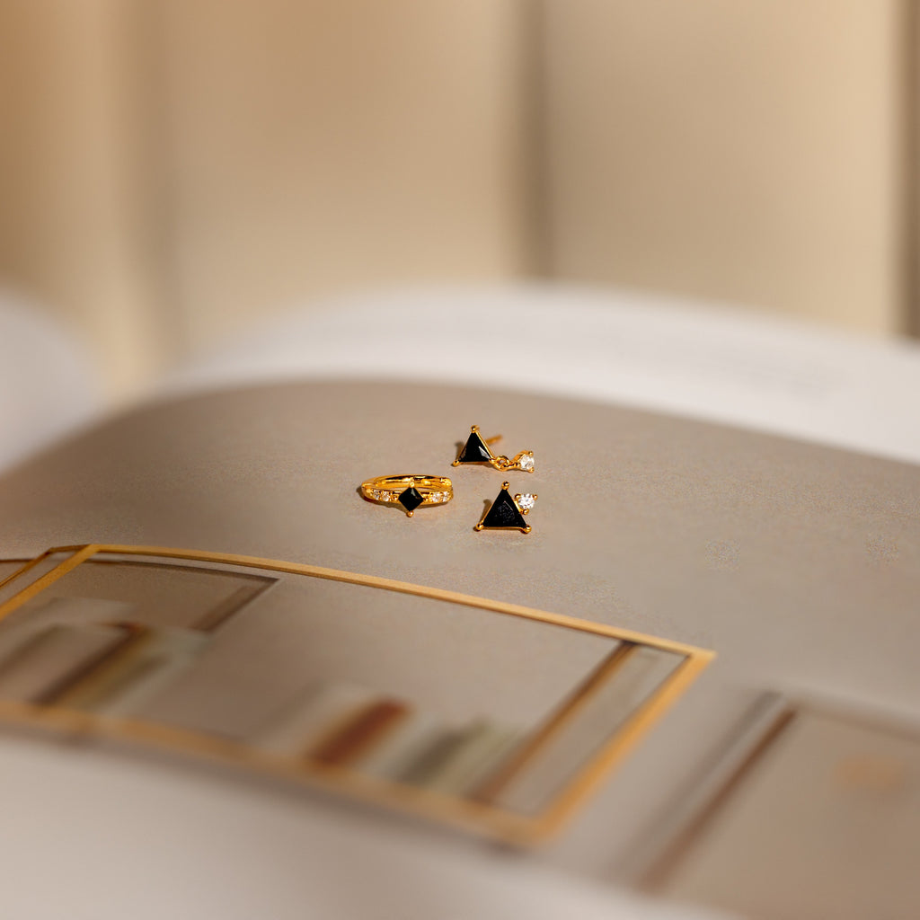 The Black Art Deco Earrings Set with geometric triangle stones rests on an open book, showcasing the timeless elegance of minimalist jewelry against a softly blurred background.
