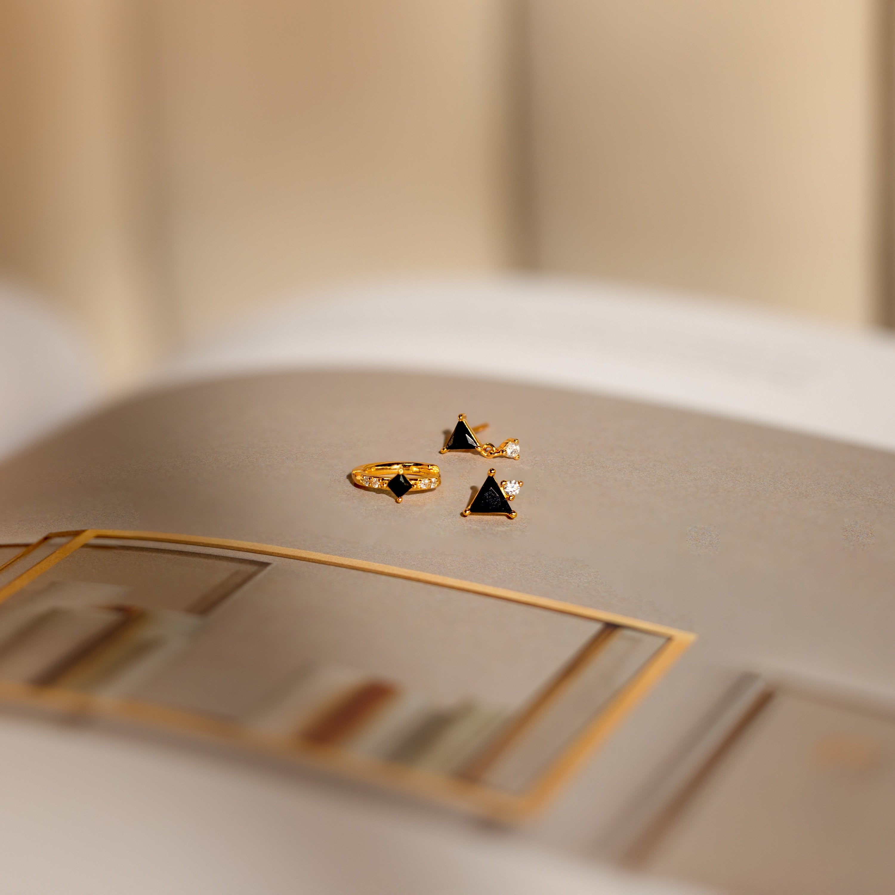 The Black Art Deco Earrings Set with geometric triangle stones rests on an open book, showcasing the timeless elegance of minimalist jewelry against a softly blurred background.