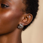 Close-up of a person's ear adorned with multiple silver earrings, including a hoop, a wave-shaped earring, and the Bold Triple Knot Studs featuring a rope-like textured design for added dimension.