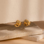 Bold Triple Knot Studs are showcased on textured stone slabs, highlighting their rope-like design against a neutral background.