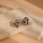 The Bold Triple Knot Studs, featuring a rope-inspired design, are displayed elegantly on a stone.