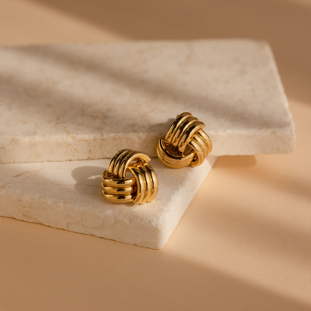 Bold Triple Knot Studs featured on stacked stone slabs under soft beige lighting and shadows, highlighting their chic rope-inspired design.