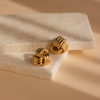 Bold Triple Knot Studs featured on stacked stone slabs under soft beige lighting and shadows, highlighting their chic rope-inspired design.