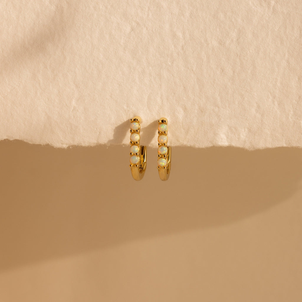 Opal Link Hoops—gold hoops adorned with small white stones, echoing the look of delicate opal earrings—are shown on a textured beige surface with soft shadow.