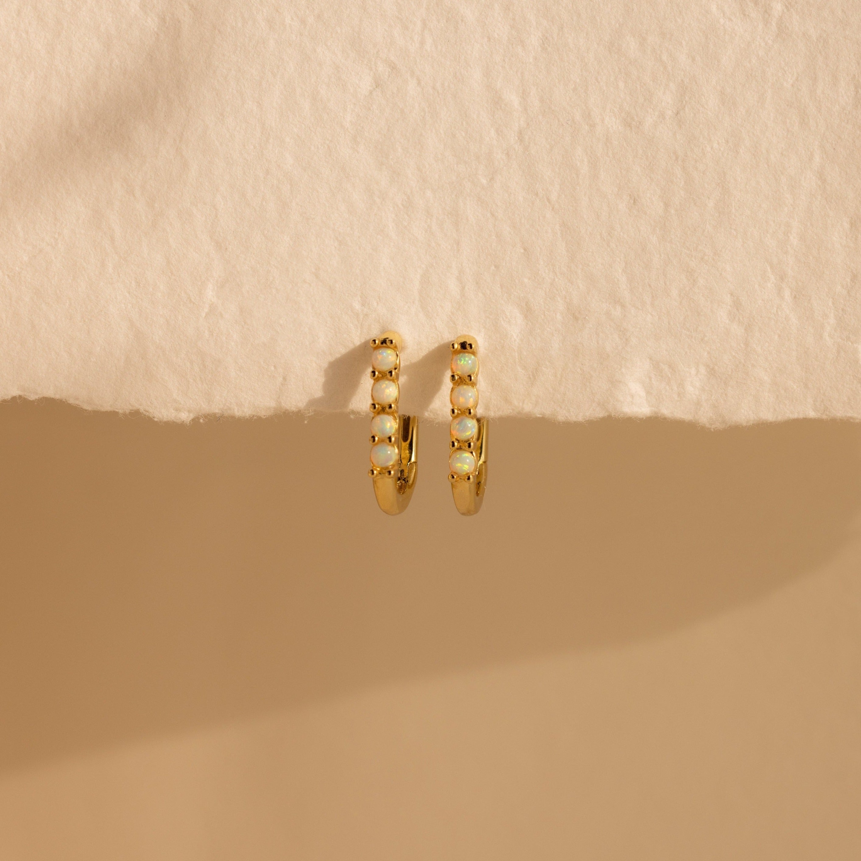 Opal Link Hoops—gold hoops adorned with small white stones, echoing the look of delicate opal earrings—are shown on a textured beige surface with soft shadow.