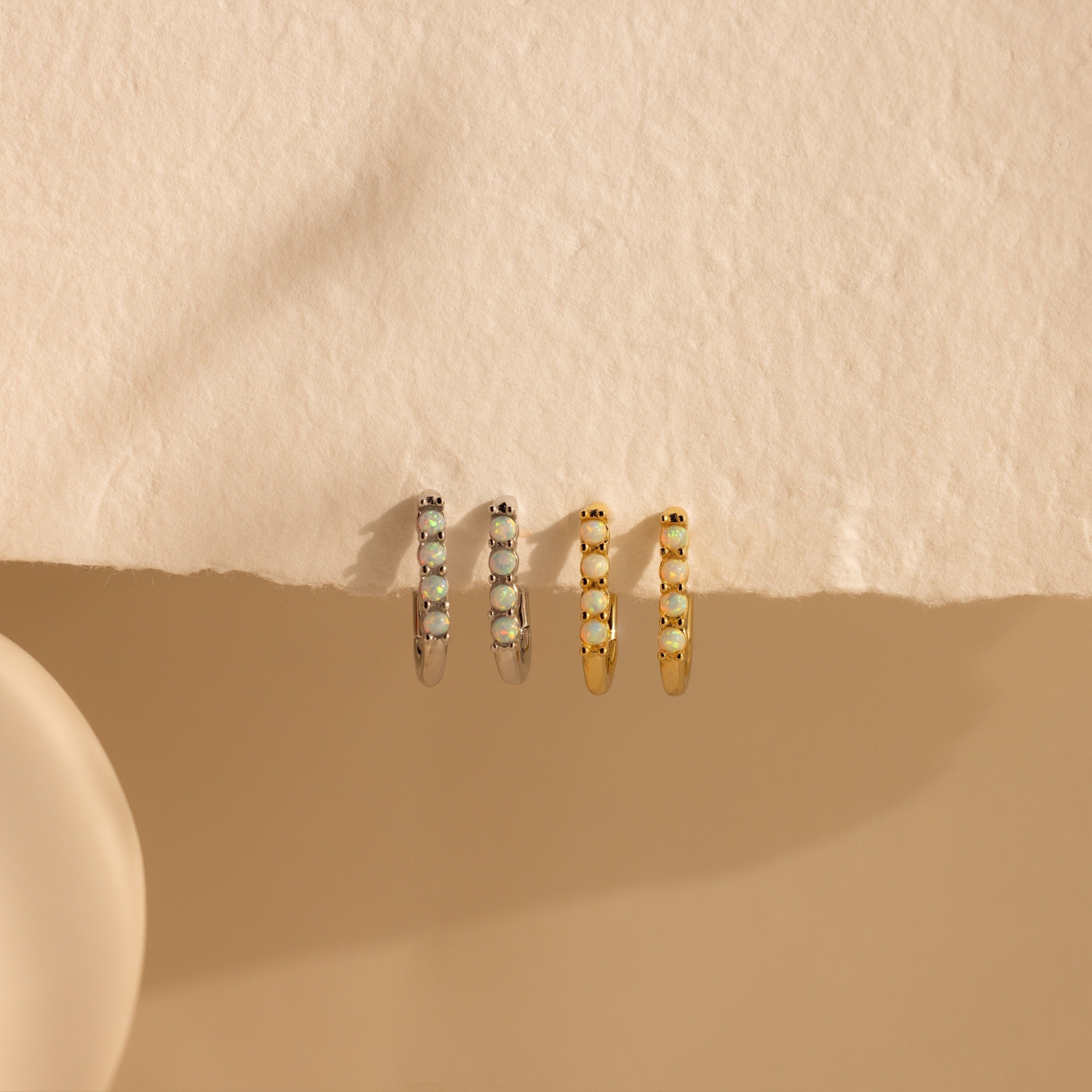 Two pairs of Opal Link Hoops—one silver pair with gemstone accents and one gold pair—are showcased on textured beige paper.