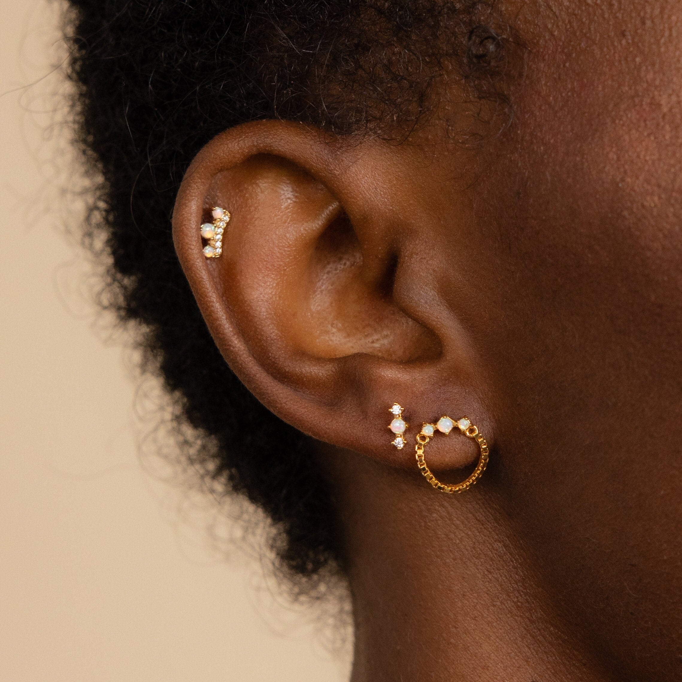 Close-up of an ear wearing the Opal Cartilage Studs Set: three gold and diamond earrings—a hoop, a stud, and an upper ear cuff—showcasing trendy helix piercings.