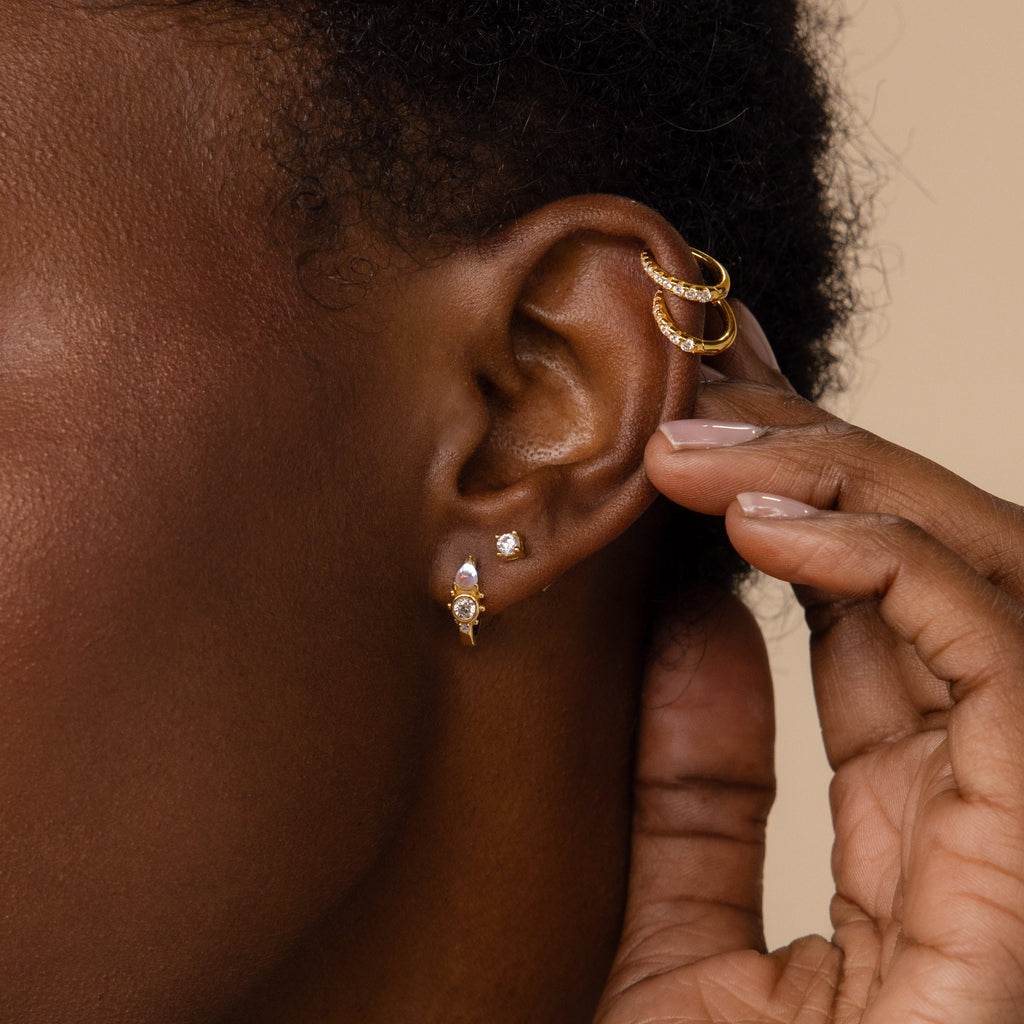 A close-up of a person's ear adorned with multiple Opal and Diamond Huggies, as a hand gently touches the ear.