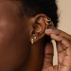 A close-up of a person's ear adorned with multiple Opal and Diamond Huggies, as a hand gently touches the ear.