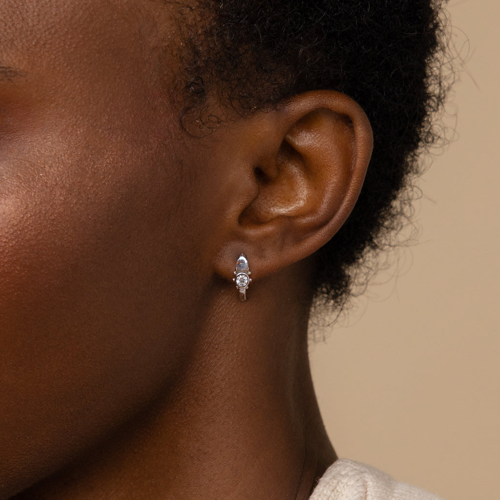 Close-up of a woman's ear wearing Opal and Diamond Huggies, small silver hoop earrings accented with a round gemstone, showcasing the refined elegance of minimalist jewelry.