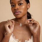 A woman in a lace top displays the Sun & Moon Tarot Necklace against a beige background, highlighting this statement jewelry's celestial charm.