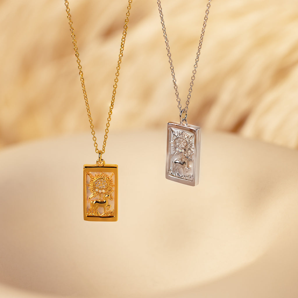 The Sun & Moon Tarot Necklace comes in gold and silver, featuring embossed animal and sun designs—stunning statement pieces that stand out against a soft beige background.