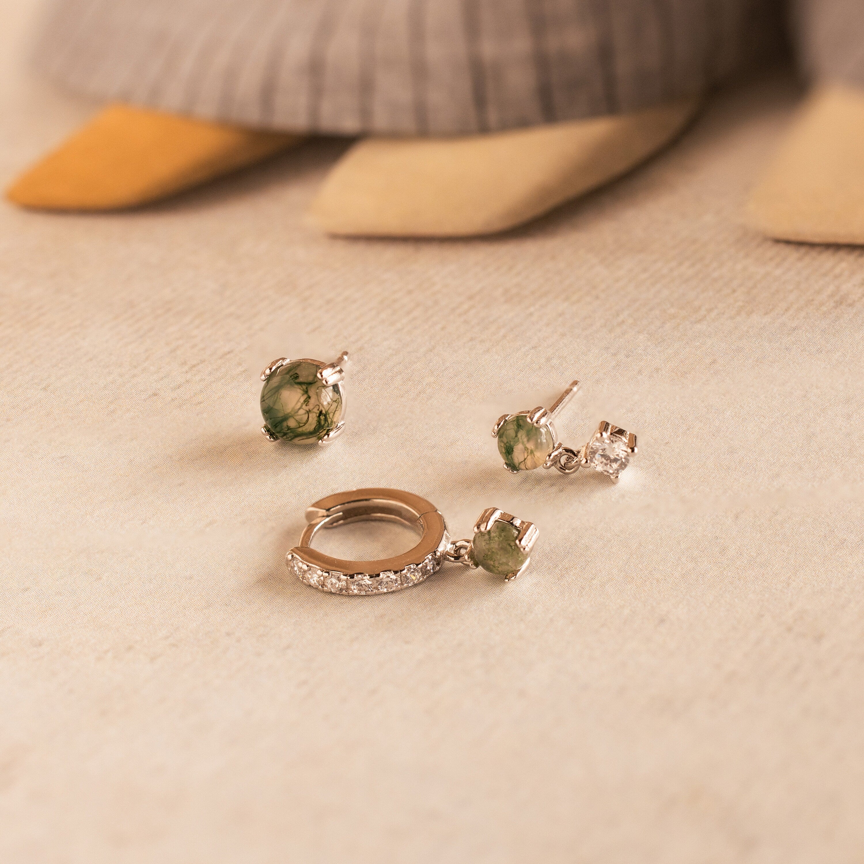 The Agate Earrings Set features three silver pieces with green and clear stones, beautifully displayed on beige fabric—perfect for mixing into your favorite jewelry collections.