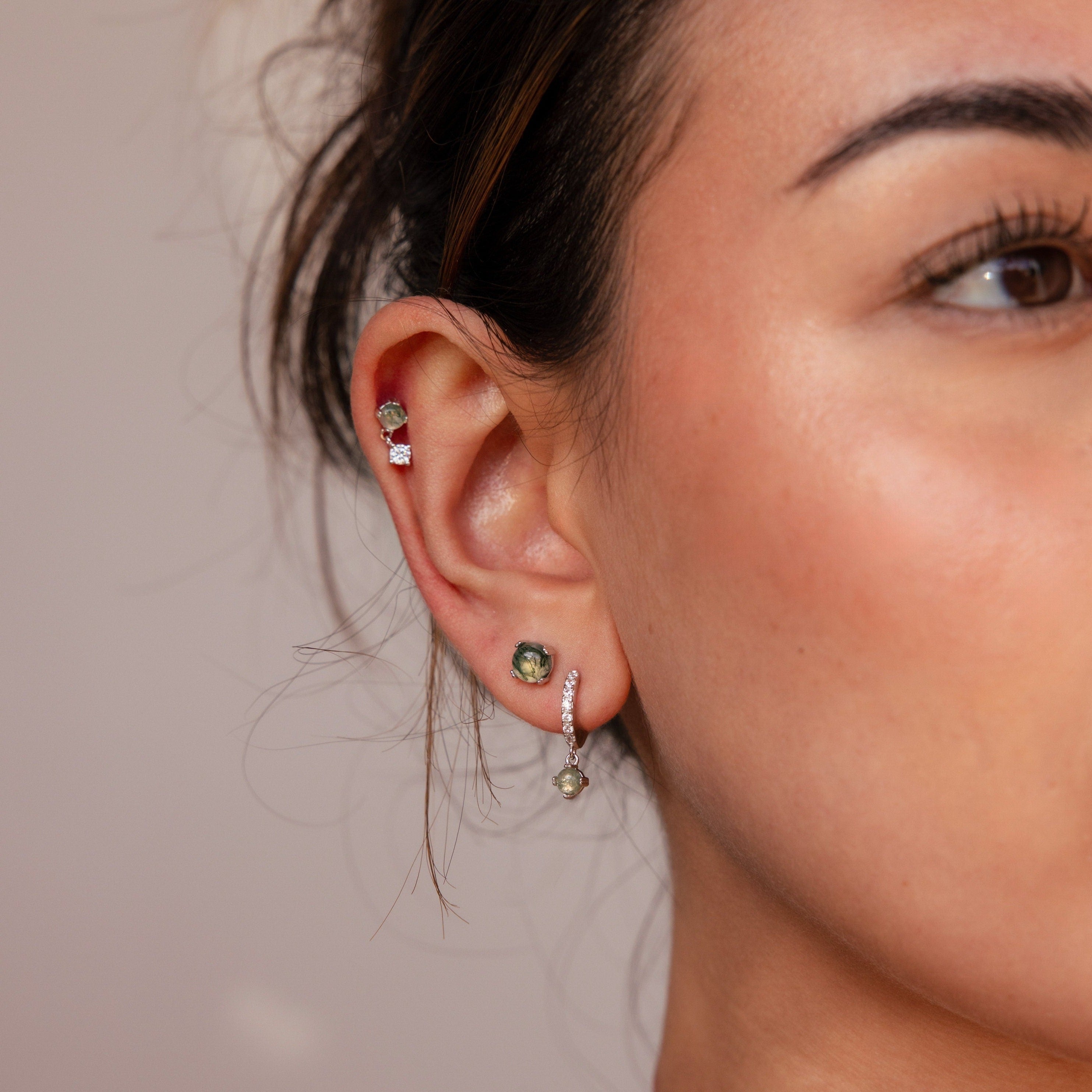 Close-up of a woman's ear wearing the Agate Earrings Set, featuring a red stud, green stud, and a dangling green earring.