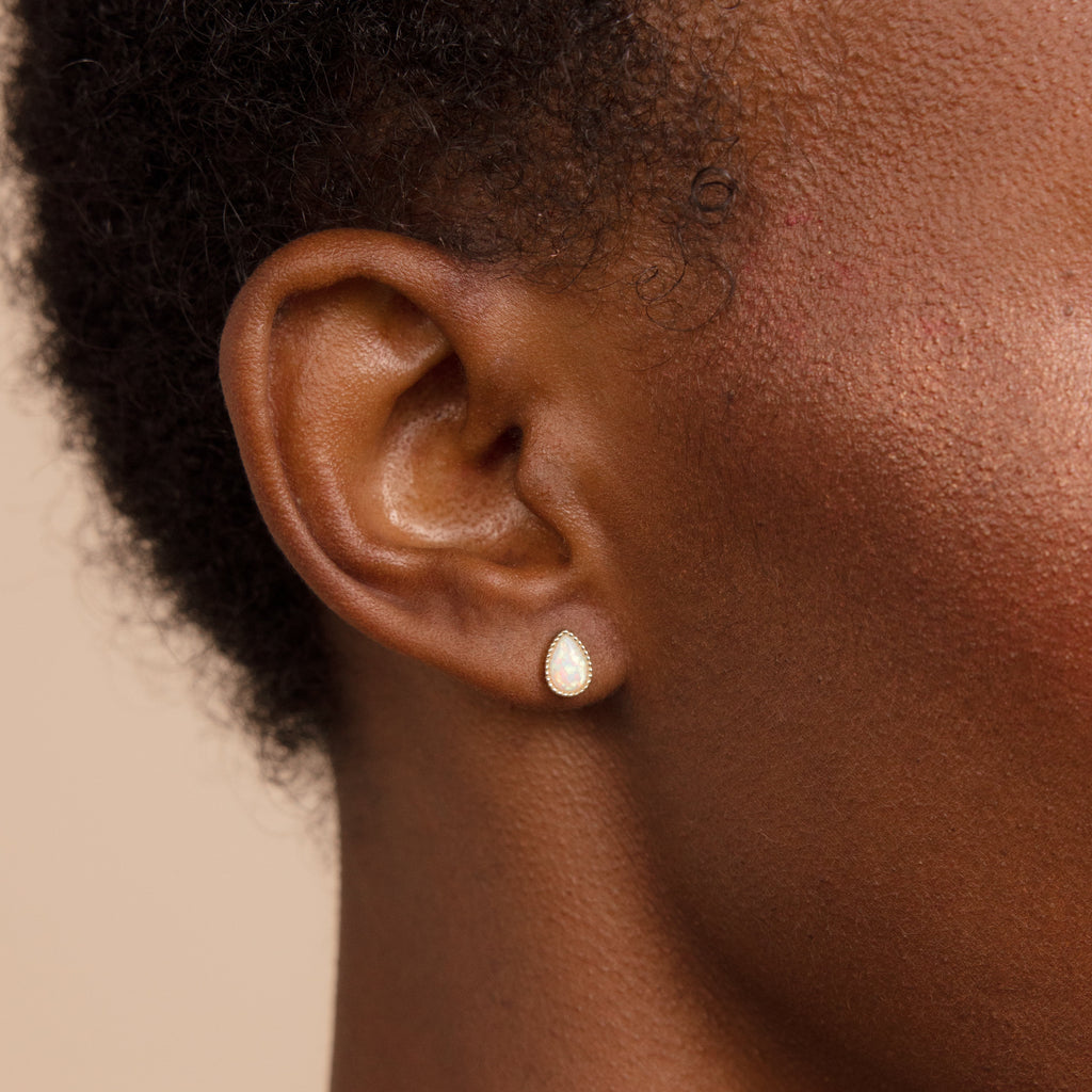 Close-up of a person’s ear adorned with Opal Teardrop Studs—a delicate, teardrop-shaped earring featuring a white opal stone, perfect for bringing vintage-inspired charm to any look.