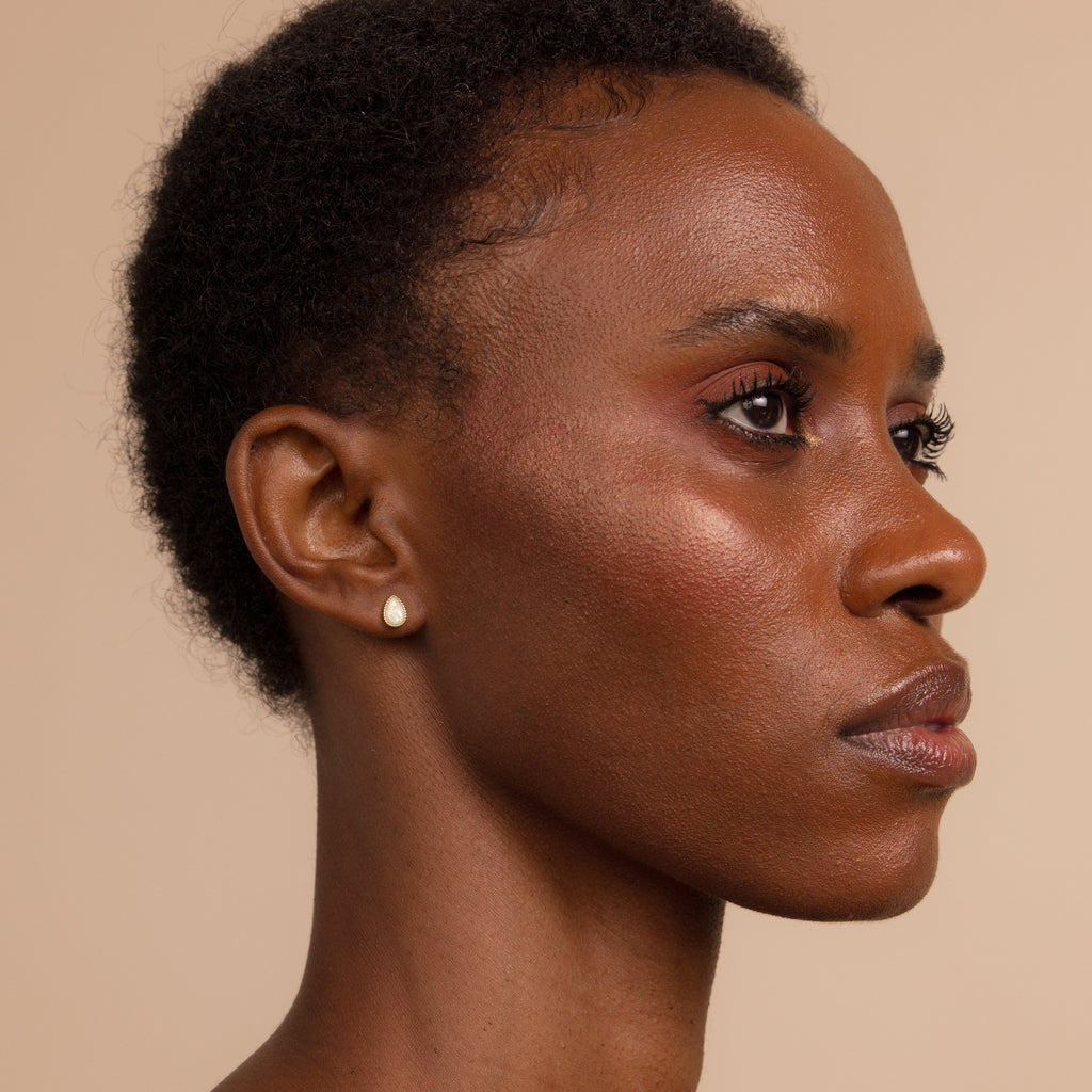 A woman with short hair and Opal Teardrop Studs looks to the side against a beige background, her style elevated by vintage-inspired jewelry.