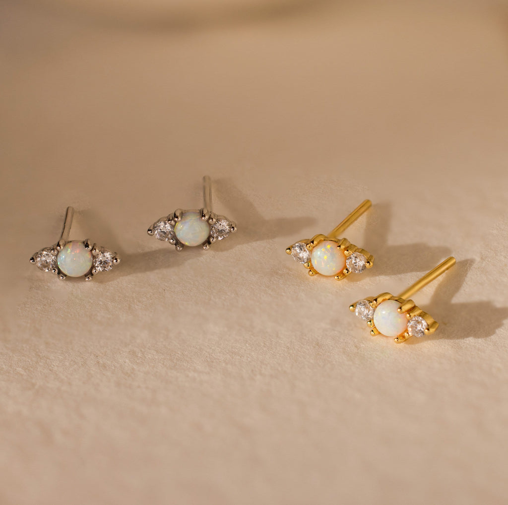 Two pairs of Opal and Diamond Studs, ideal for cartilage or helix piercings—one set silver, one set gold—displayed elegantly on a beige surface.