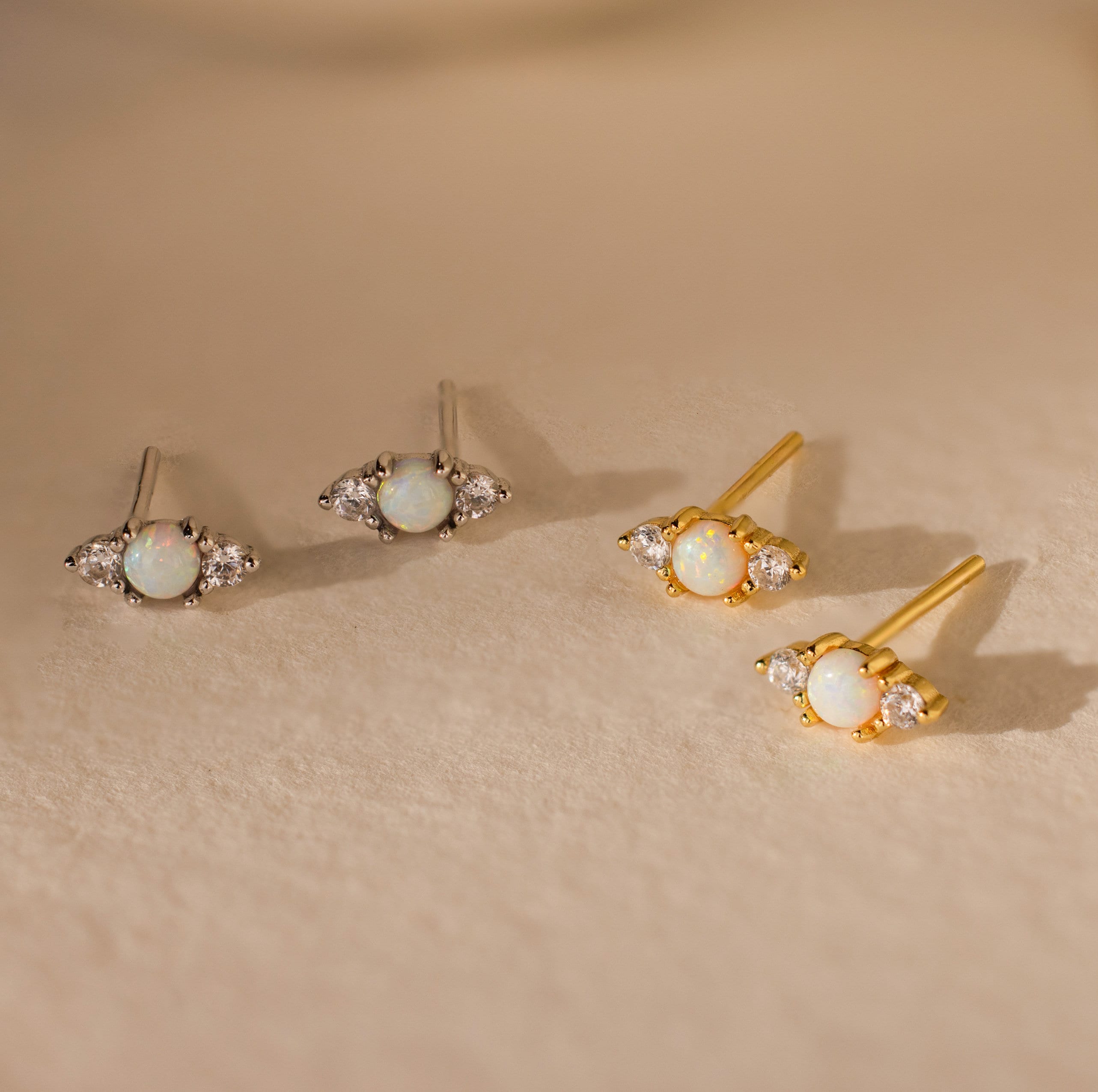 Two pairs of Opal and Diamond Studs, ideal for cartilage or helix piercings—one set silver, one set gold—displayed elegantly on a beige surface.