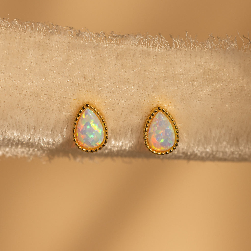 Opal Teardrop Studs with gold trim, shown on textured beige fabric, bring vintage-inspired elegance to any outfit.