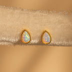 Opal Teardrop Studs with gold trim, shown on textured beige fabric, bring vintage-inspired elegance to any outfit.