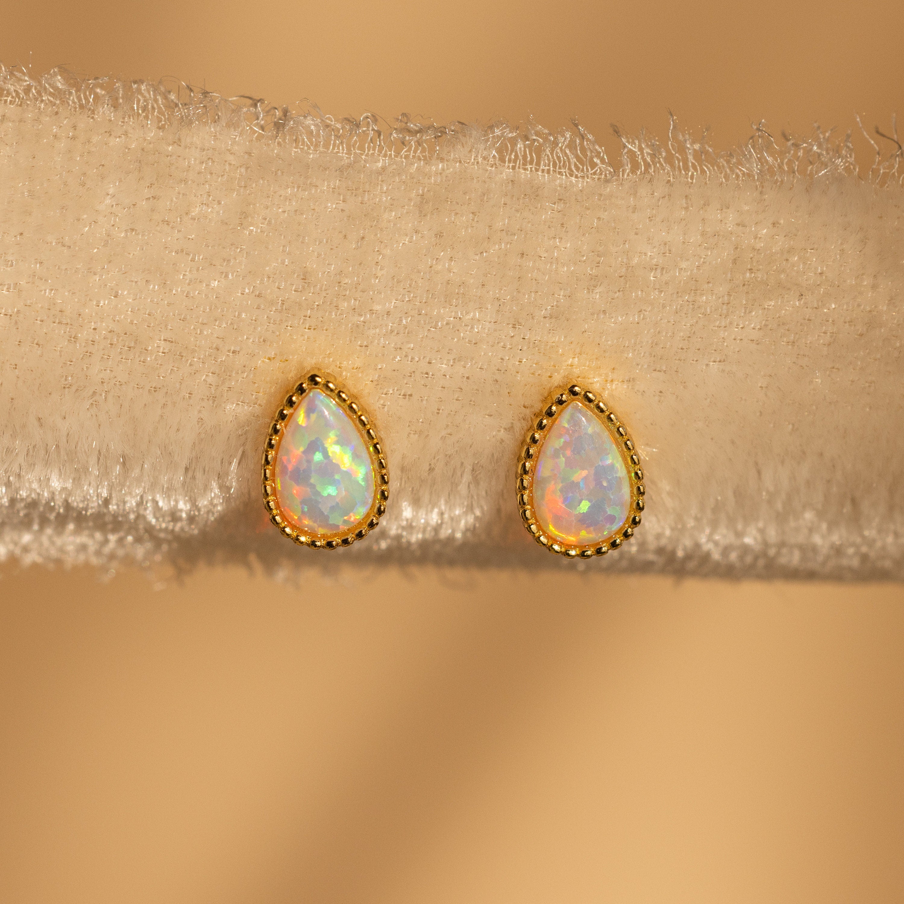 Opal Teardrop Studs with gold trim, shown on textured beige fabric, bring vintage-inspired elegance to any outfit.