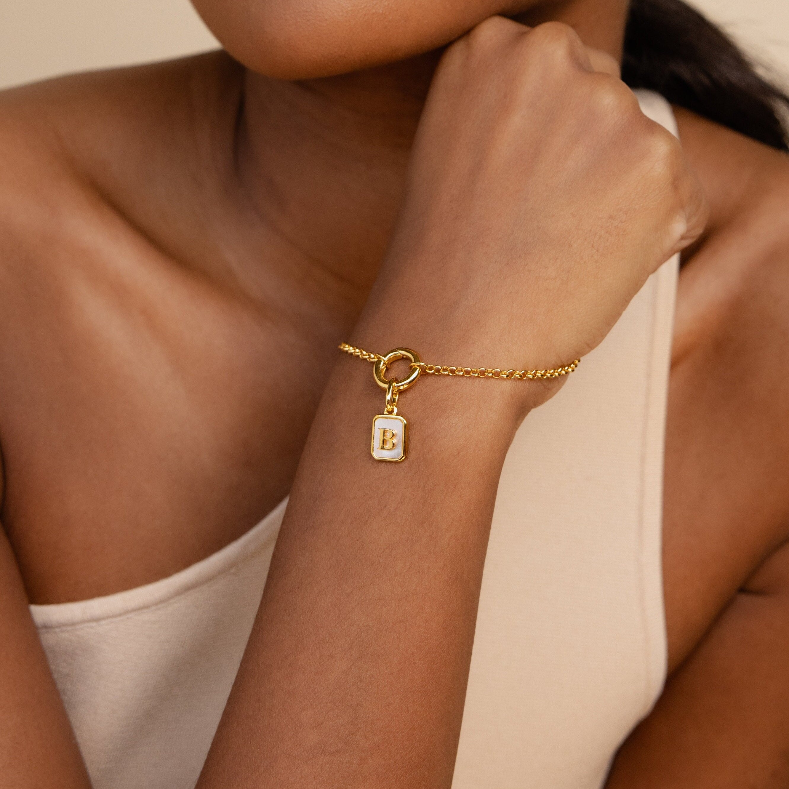 Model wearing a rolo circle bracelet with a dangling gold mother of pearl initial B charm