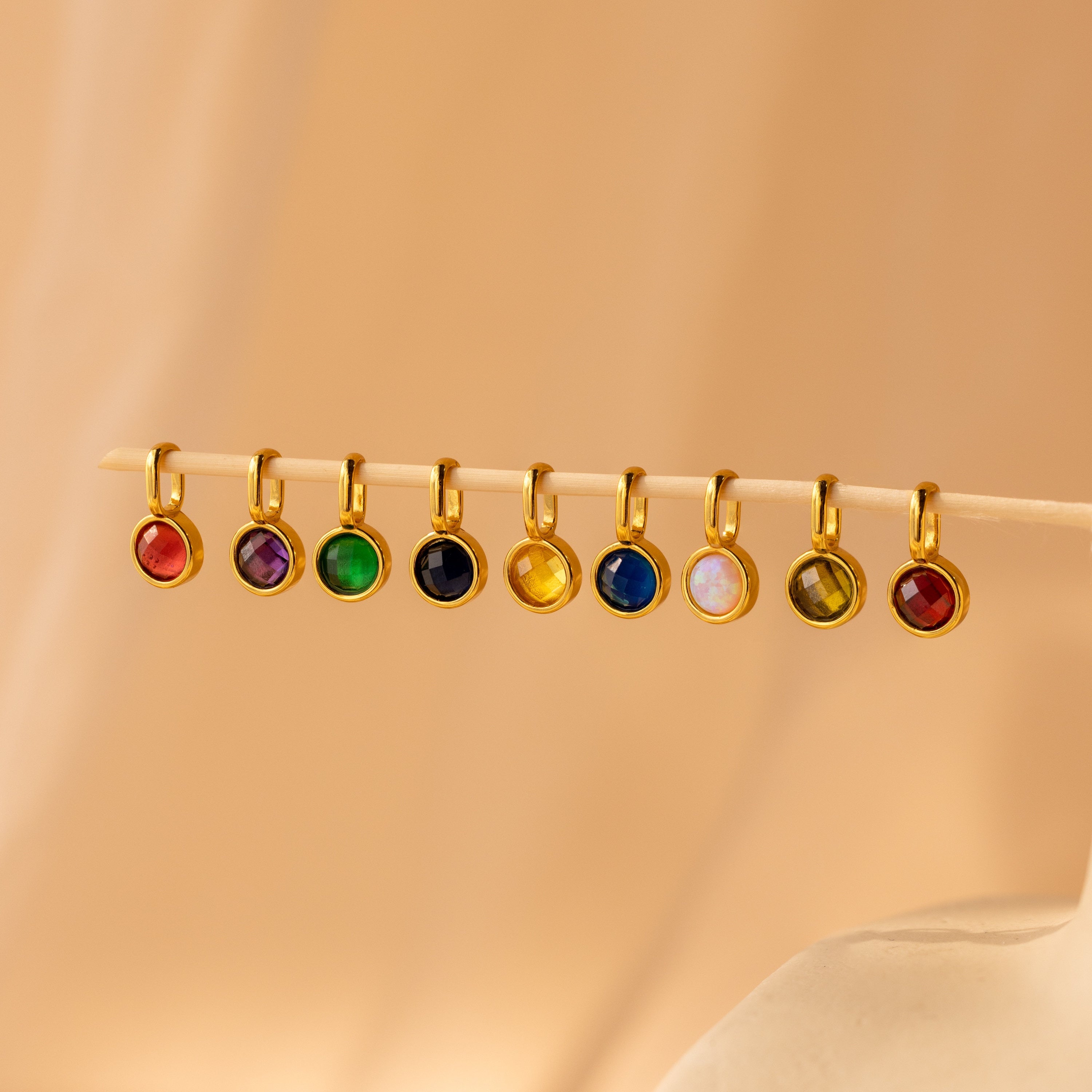 Several signet birthstone charms spaced out alongside a  wooden dowel