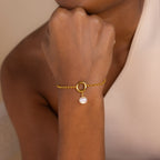 A person wearing the Classic Pearl Charm in Sterling Silver as a bracelet, featuring a circular charm and a single dangling pearl, paired with a delicate hoop earring.
