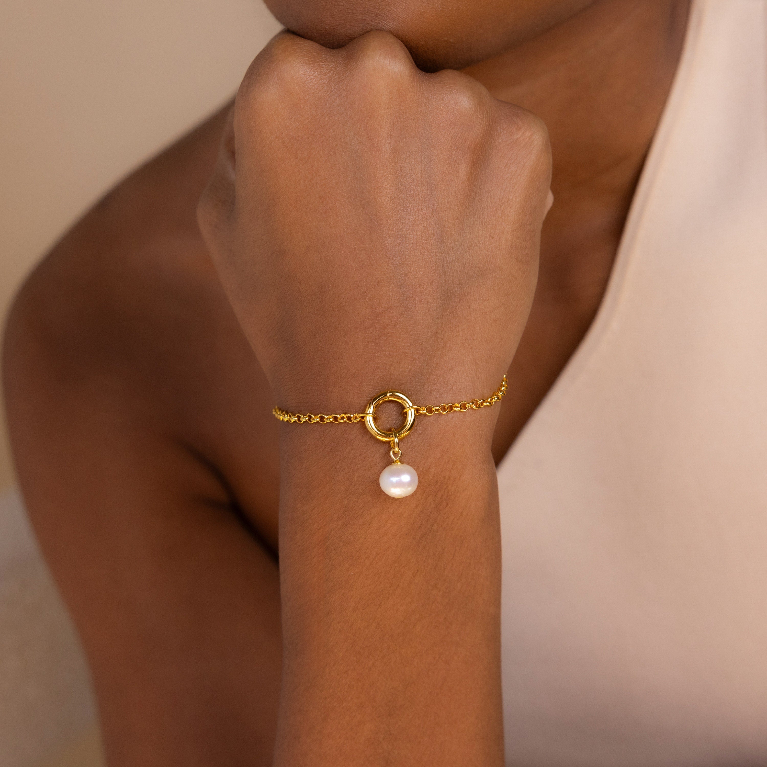 A person wearing the Classic Pearl Charm in Sterling Silver as a bracelet, featuring a circular charm and a single dangling pearl, paired with a delicate hoop earring.