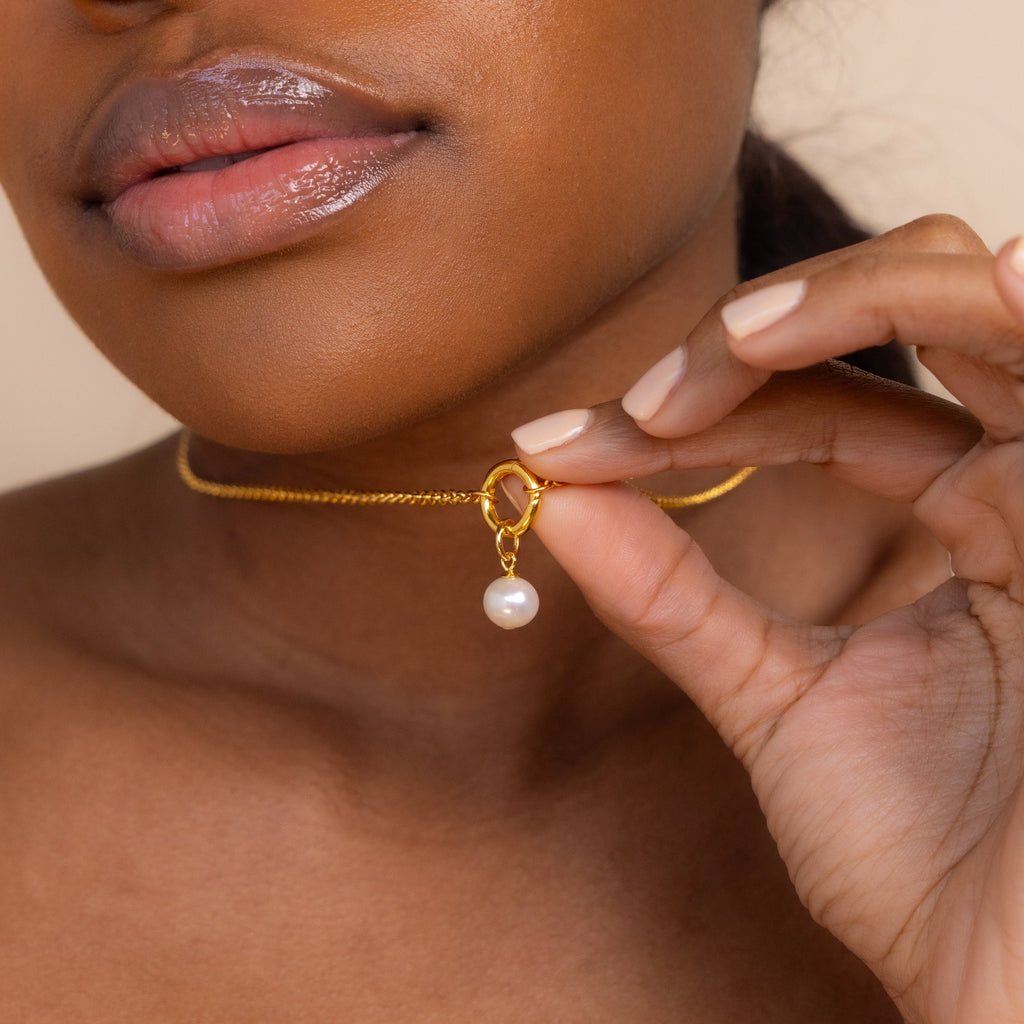 Woman holding the Classic Pearl Charm in Sterling Silver close to her neck, highlighting her glossy lips and nude nails.
