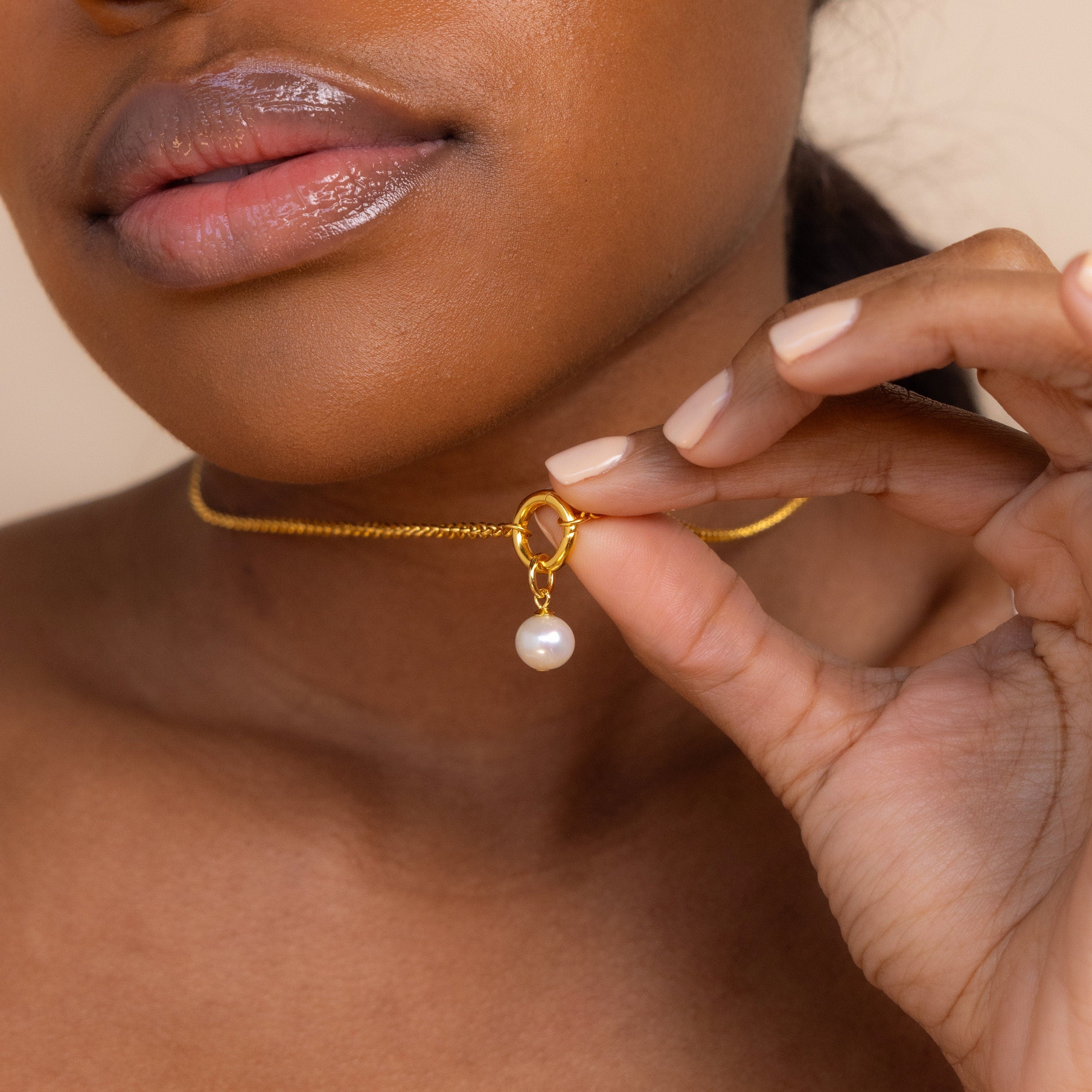 Woman holding the Classic Pearl Charm in Sterling Silver close to her neck, highlighting her glossy lips and nude nails.
