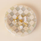 An assortment of different pearl, birthstone and vintage charms with jump rings on a checkerboard dish