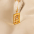 The Sun & Moon Tarot Necklace features a gold rectangular pendant engraved with a sun, moon, rays, and a figure, set against a soft beige background—ideal for those who love statement jewelry.