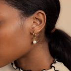 Close-up of an ear wearing the Classic Pearl Charm in Sterling Silver, a delicate hoop earring with a pearl detail, on a person with dark hair pulled back.