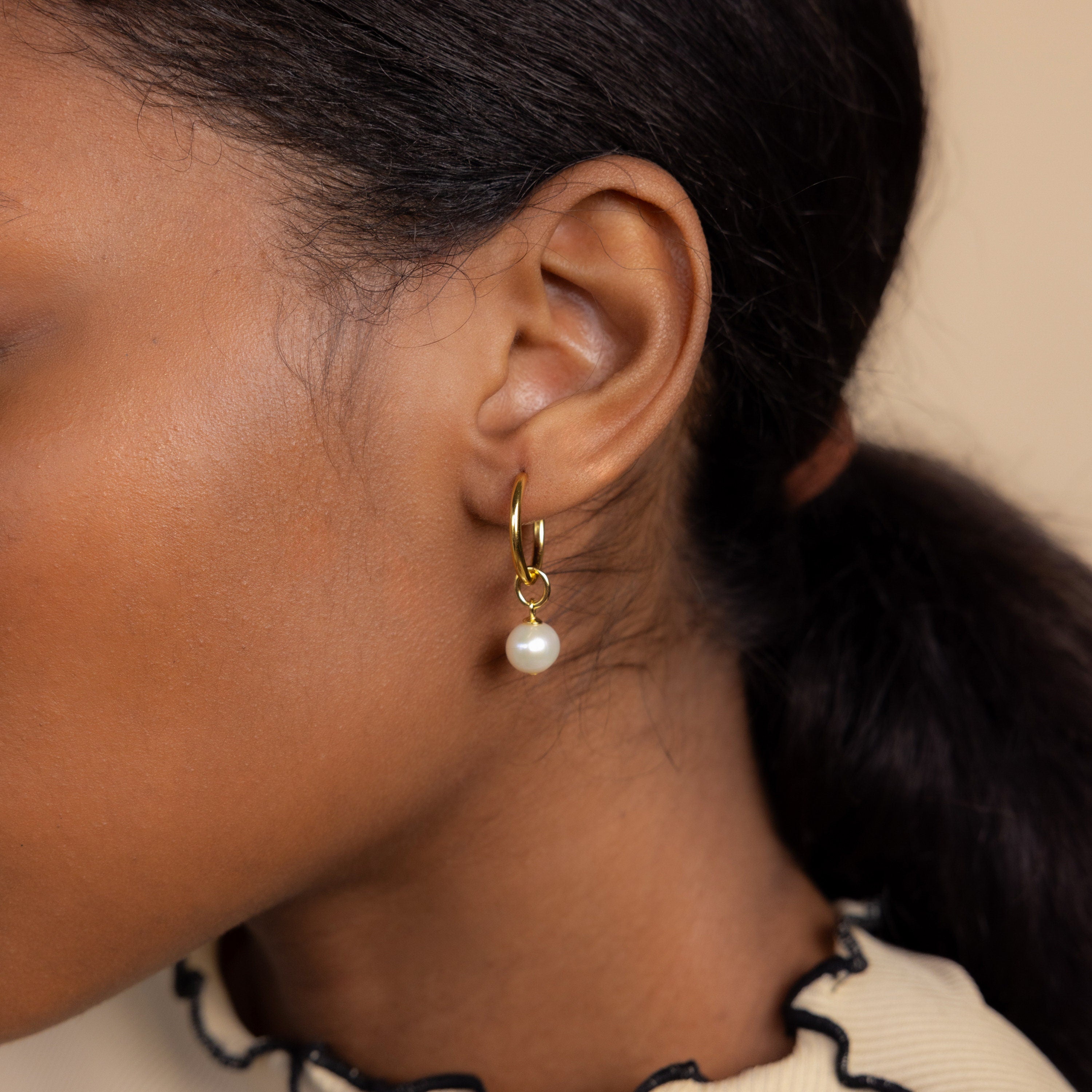 Close-up of an ear wearing the Classic Pearl Charm in Sterling Silver, a delicate hoop earring with a pearl detail, on a person with dark hair pulled back.