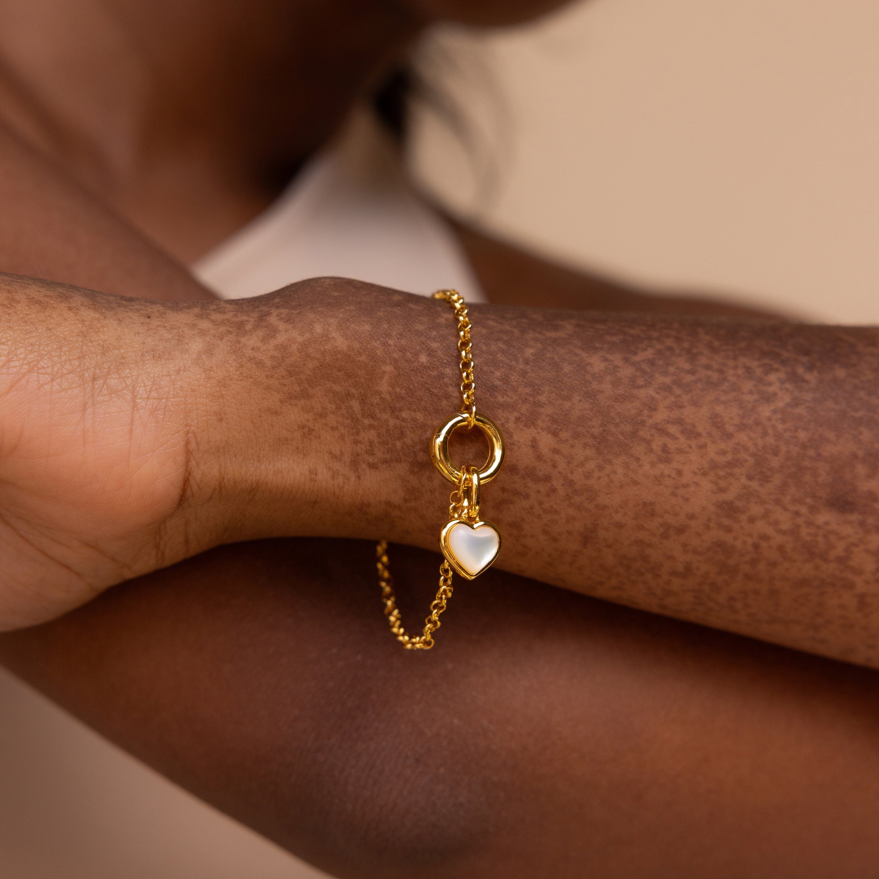 The Mother of Pearl Heart Charm in 18K Gold rests on a wrist with vitiligo, blending elegance and vintage charm.