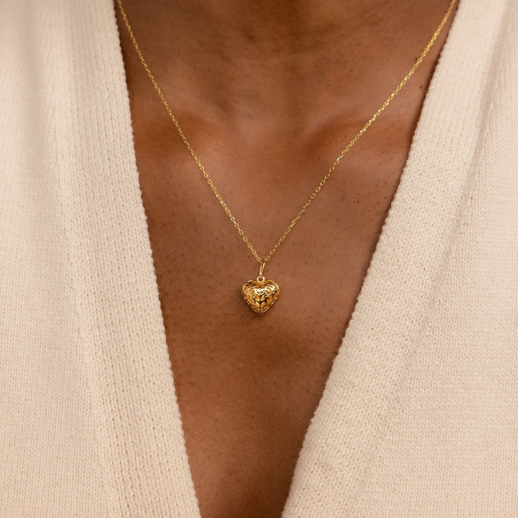 The Vintage Heart Charm, a gold heart-shaped pendant necklace from our collection, pairs perfectly with a cream-colored V-neck knit top.