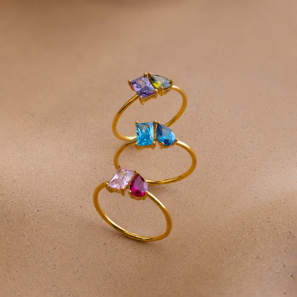 The Toi et Moi Birthstone Ring, a customizable gold ring with colorful gemstones, stacked on sand—an elegant Christmas gift.
