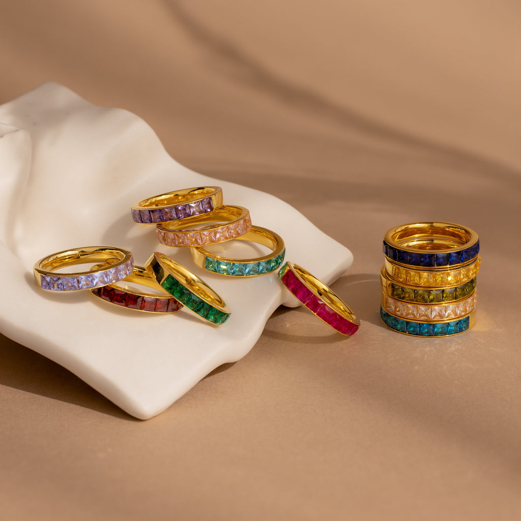 The Birthstone Inlay Band is displayed on a white surface and stacked on a beige background, highlighting each ring as a unique birthstone accessory and bold statement piece.