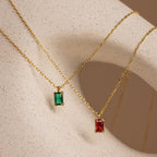 Two Emerald Cut Birthstone Necklaces with rectangular green and red gemstone pendants are displayed on a beige speckled surface—stunning, customizable, and the perfect Christmas gift.