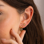 Close-up of a woman’s ear wearing mystical jewelry, including Labradorite Hexagon Studs and two additional gold earrings, as her hand gently touches her cheek.