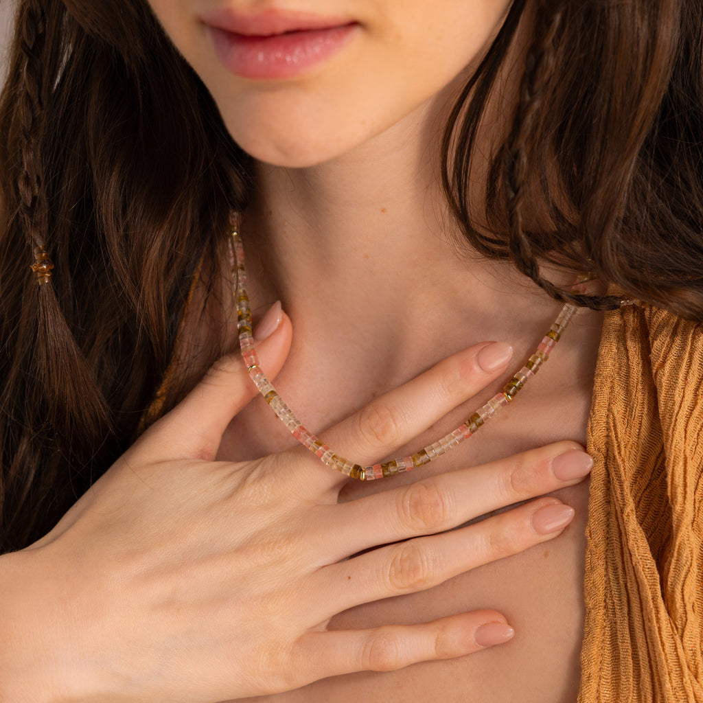 Close-up of a woman wearing the Rose Quartz Beaded Necklace, gently touching her chest while in a mustard-yellow top—a meaningful gift for your best friend.
