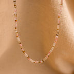 The Rose Quartz Beaded Necklace features pink, clear, and gold beads and is shown on a soft beige fabric background—a thoughtful gift for your best friend.