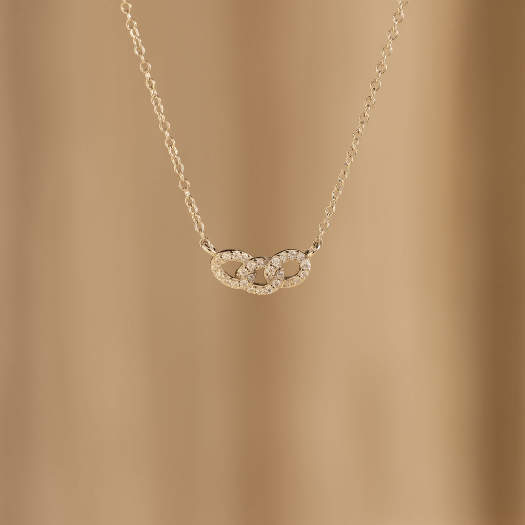 The Pave Link Necklace features two interlocking, diamond-studded circles on a soft beige background—a stunning addition to any jewelry collection.
