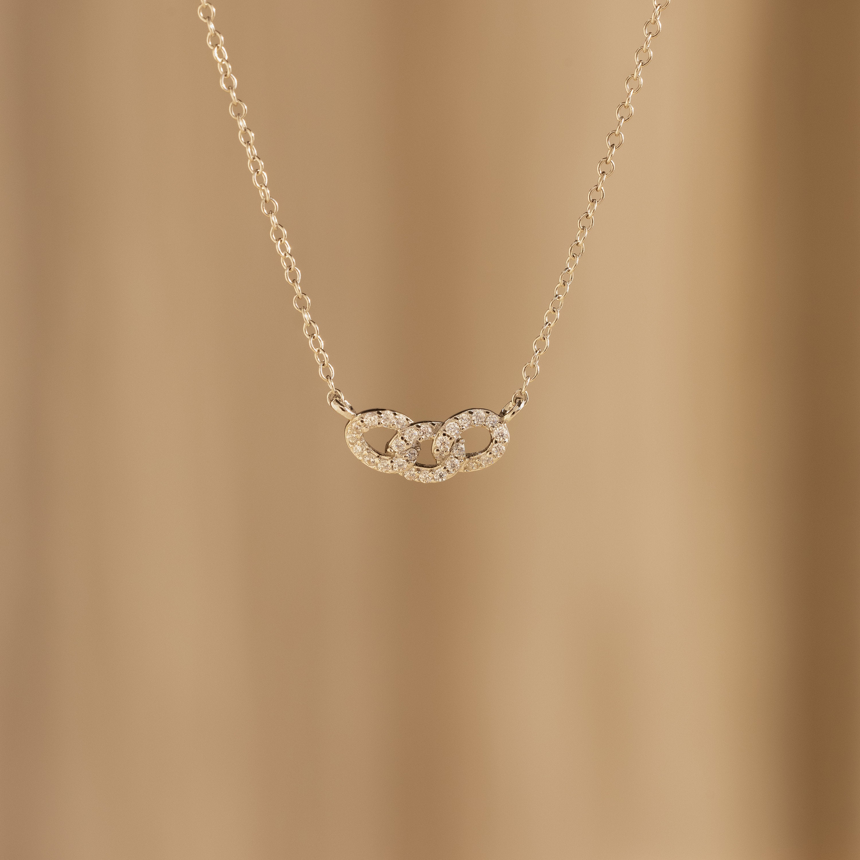The Pave Link Necklace features two interlocking, diamond-studded circles on a soft beige background—a stunning addition to any jewelry collection.