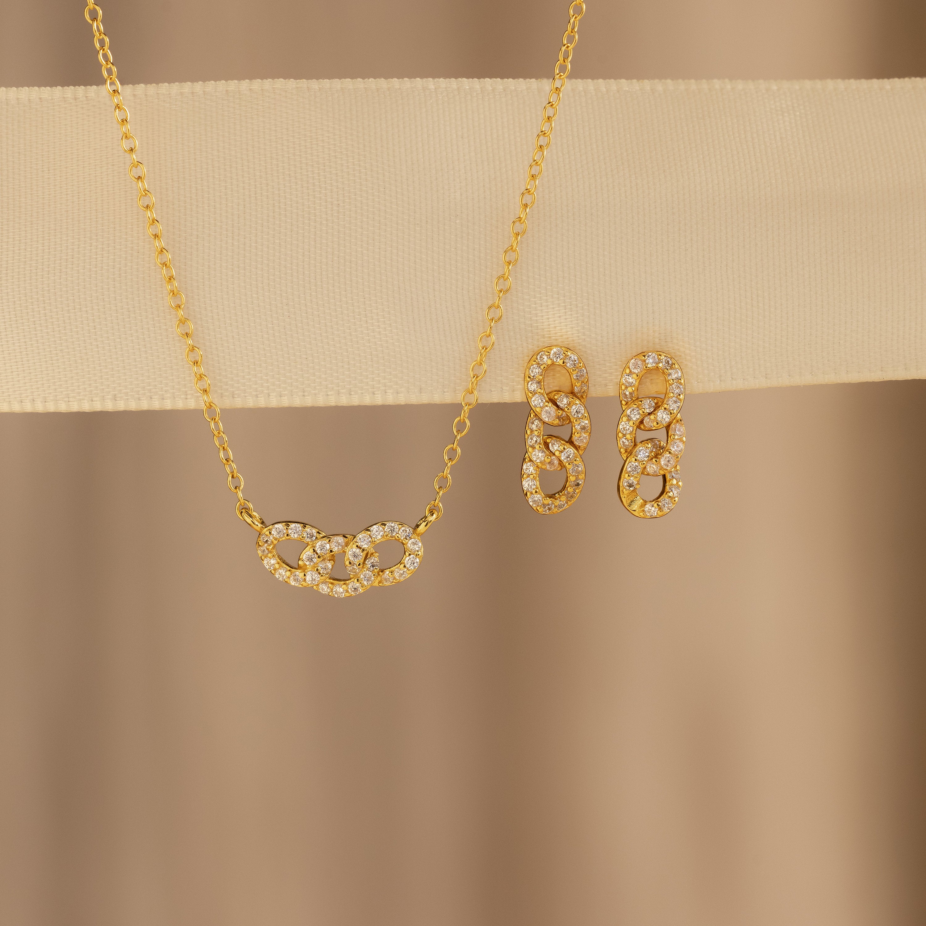 Pave Link Necklace and matching earrings with interlocking, diamond-studded oval links from our collection, shown on a beige background.