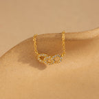 The Pave Link Necklace showcases two diamond-studded interlocking links on a gold chain, elegantly presented on a beige surface—a stunning addition to any jewelry collection.