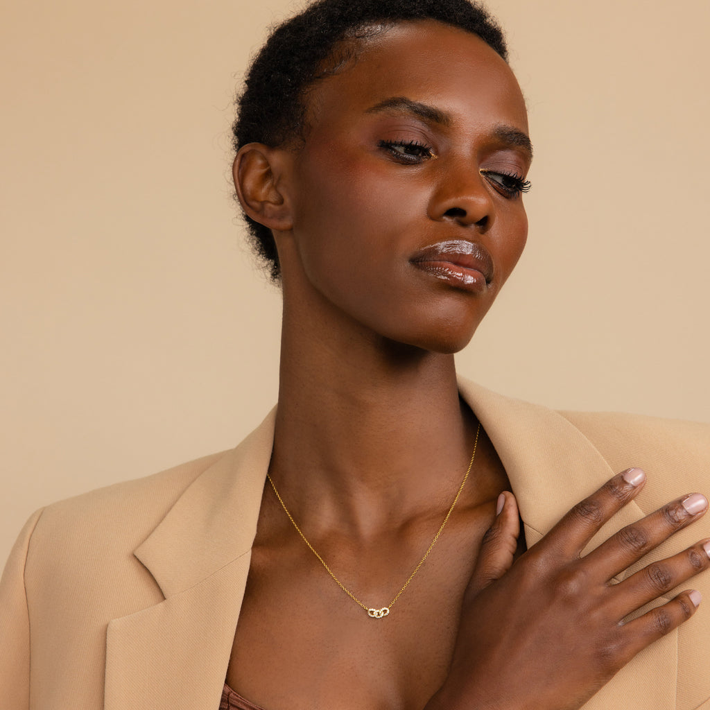 A woman wearing the Pave Link Necklace, featuring gold interlocking links, looks to the side against a neutral background—highlighting this standout piece from the collection.